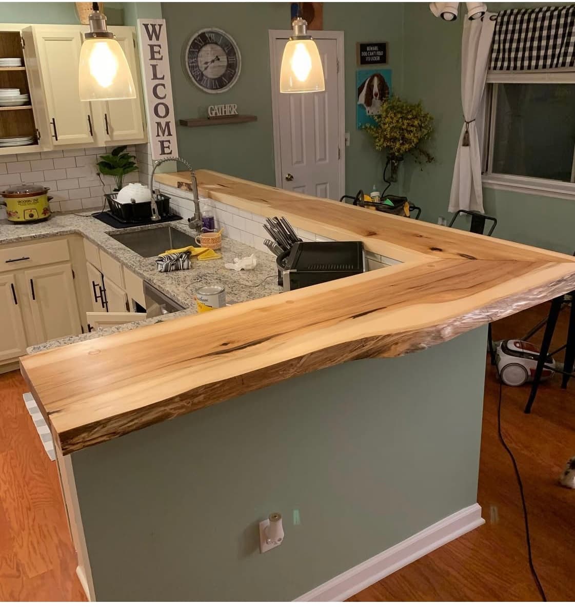 Live edge bar countertop installed in an L-shaped kitchen with light cabinets and warm light